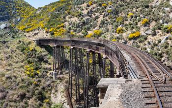 Railway track of Taieri Gorge tourist railway crosses a steel trestle bridge across a ravine on its journey up the valley