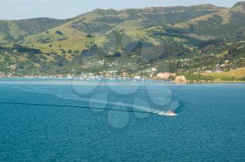 Lifeboat Tender from cruise ship approaching boat with yachts moored in Akaroa Harbor in New Zealand with the town and pier in the distance