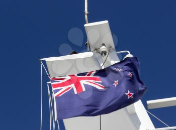 Flag of New Zealand flutters by white mast and funnel of large ship