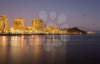 Panorama of the nightime skyline of Honolulu and Waikiki from Ala Moana park after the sun sets with lights illuminating the facades of the hotels and apartments