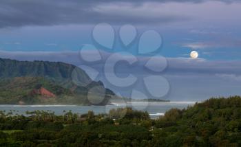 Bay at Hanalei in Kauai with the Na Pali mountain range in the background. Taken just after dawn with the moon setting behind clouds on the horizon