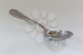 Decorated slotted serving or dessert spoon for draining wet vegetables in side view on fine white tablecloth with pattern just visible