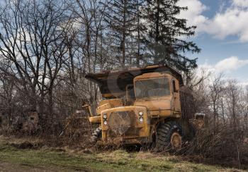 Rusting and overgrown heavy yellow industrial truck and equipment abandoned in economic recession
