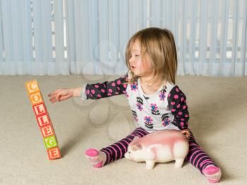 Young girl on floor of home saving money in a piggy bank for college educational expenses that will be out of reach in the future
