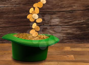 Treasure of pure gold coins pouring down onto a green velvet hat on wooden table. Concept image to celebrate luck on St Patrick's Day of March 17th
