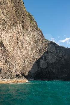 Cave entrance in rocky shore of Na Pali coastline from sunset cruise boat trip