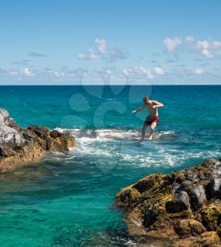 Dangerous leap into warm blue ocean off rocks at Lumahai Beach on Hawaiian island of Kauai