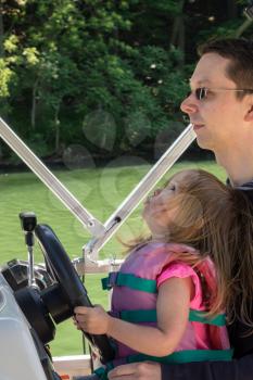 Father and young daughter driving a speedboat on a lake in summer while wearing a life jacket
