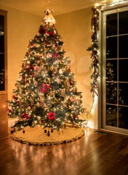 Ornately decorated christmas tree in the corner of a modern living room illuminated only by its lights