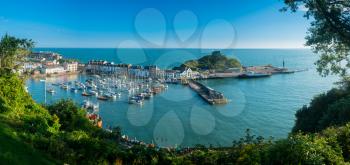 Ilfracombe Harbor at sunrise in broad panorama across the picturesque town.
