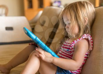 Young girl sitting at home on settee and using a child's tablet touch screen computer