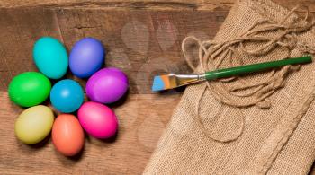 Easter background with organic eggs arranged in a flower shape on rustic wooden table with paintbrush and paint