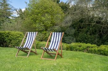 Two british deckchairs with striped cloth in an English garden in summer