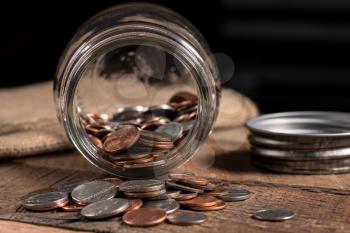 Poverty concept image with a few small coins remaining in a glass savings jar on wooden table