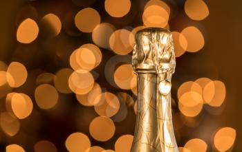 Bokeh lights from Christmas tree behind the gold foil covered neck of champagne bottle