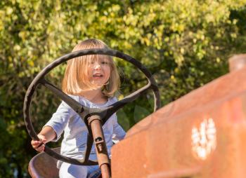 Young caucasian girl sitting on old tractor and pretending to drive