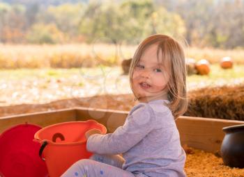 Young caucasian girl playing in the seeds from corn kernels with buckets and spade at halloween pumpkin patch