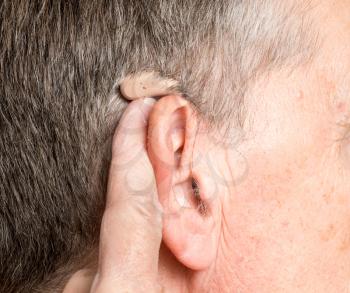 Macro close up of tiny modern hearing aid placed behind the ear of senior adult man
