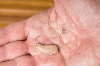 Macro close up of tiny modern hearing aid in the palm of senior adult man