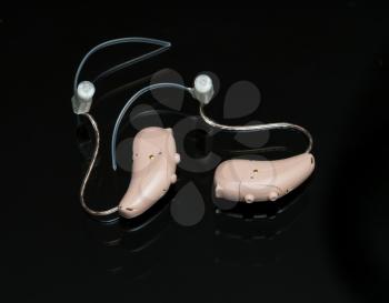 Macro close up of a matched pair of tiny modern hearing aid on black reflective background
