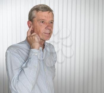 Senior caucasian man holding a tiny modern hearing aid before inserting in his ear