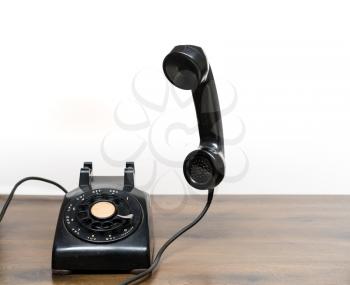 Old and antique rotary telephone on wooden desk with handset floating in the air ready for call