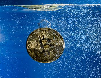 Bitcoin coin dropped into water and sinking below bubble to show the falling price of cyber currency