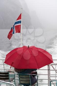 Lone passenger under umbrella on Norwegian tour ship to see Pulpit Rock near Stavanger