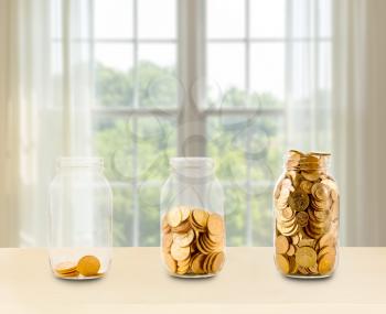 Concept of investment or savings for retirement with three glass jars filled with gold coins in front of bright window