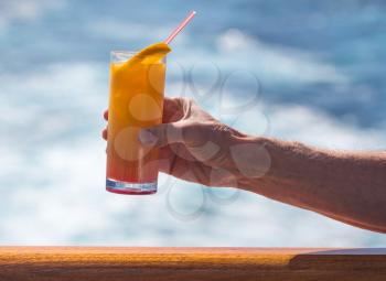 Senior caucasian adult man with tequila sunrise in glass on teak balcony rail of ocean cruise ship