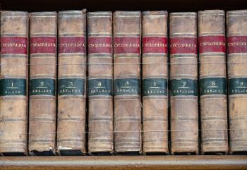 Row of old leather bound encyclopaedia books on a wooden shelf