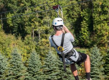 Back view of young man on zip line harness riding the zipline down between trees