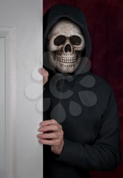 Stalker or burglar entering a home through doorway with wearing a human skull mask