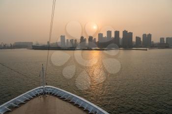 Cruise ship approaching port by large tower blocks of Qingdao in China