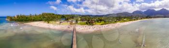 Aerial panoramic image off the coast over Hanalei Bay and pier on Hawaiian island of Kauai with surfers in the water