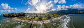 Aerial panoramic image off the coast over Hanalei Bay and pier on Hawaiian island of Kauai as the sun rises over the dramatic landscape