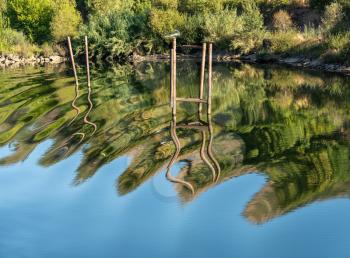 Wavy stakes and wooden poles for boat moorings and anchors reflected in calm Douro river in Portugal