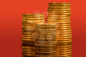 Focus on a stack of gold coins with other coin stacked in the background out of focus against red backdrop