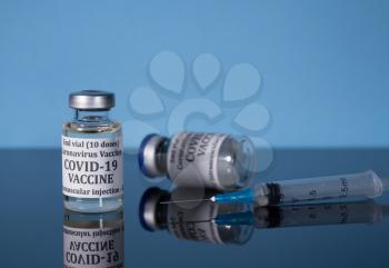 Small bottle of coronavirus vaccine on reflective glass table with syringe ready for vaccination