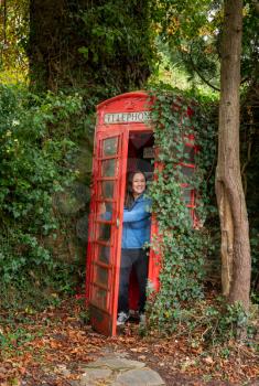 Woman opening the door from a red traditional telephone box in England