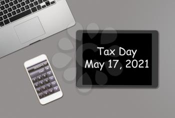 Overhead clean grey desk for laptop, smartphone and tablet computer with message for tax day 2021 as May 17