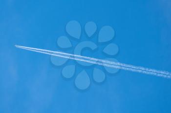 Condensation or contrail behind a two engined jet aircraft flying across blue sky in high definition image