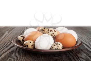 Quail and chicken eggs in a clay plate on a wooden table