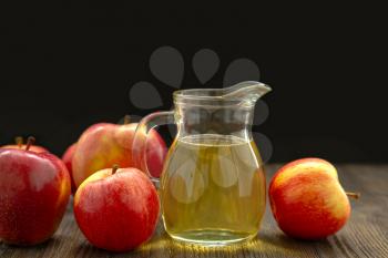 Hard apple cider in a glass jug and red ripe apples on a black background