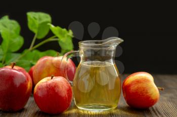 Hard apple cider in a glass jug, red ripe apples and green leaves on a black background