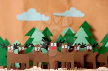 Team Reindeer Santa Claus standing in snowy forest. In front of red nosed Rudolph. The whole picture is cutting out from colored paper