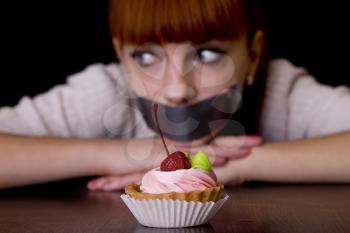 The girl, whose mouth sealed with tape sad looking at cakes