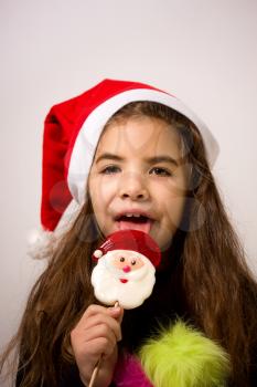 A little girl in a New Year's hat eating a candy in the form of Santa Claus