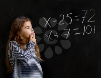 a little girl is standing near a school board and is trying to solve a difficult task for her in mathematics