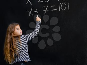 a little girl is standing near a school board and is trying to solve a difficult task for her in mathematics